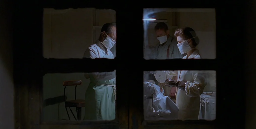 Dominion: Prequel to the Exorcist (2005) movie still: medium — An operating room view is seen through a dark, framed windowpane at night. Three…