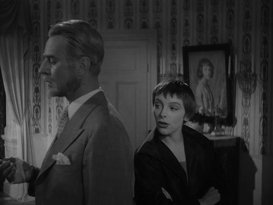 Dreams (1955) movie still: medium — A dark indoor space featuring vintage patterned wallpaper and a framed portrait on display. A man stands in…