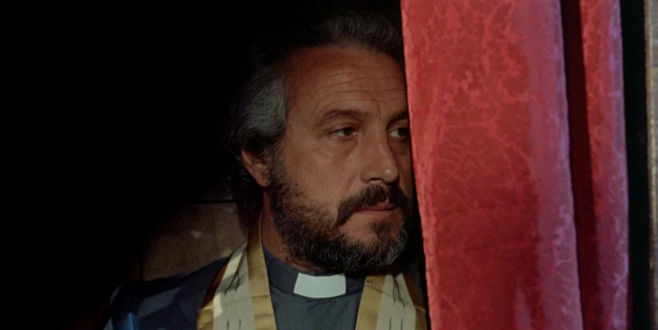 Dark Habits (1983) movie still: closeup — A man in clerical vestments rests his head against a heavy red textured curtain. The surrounding space is…