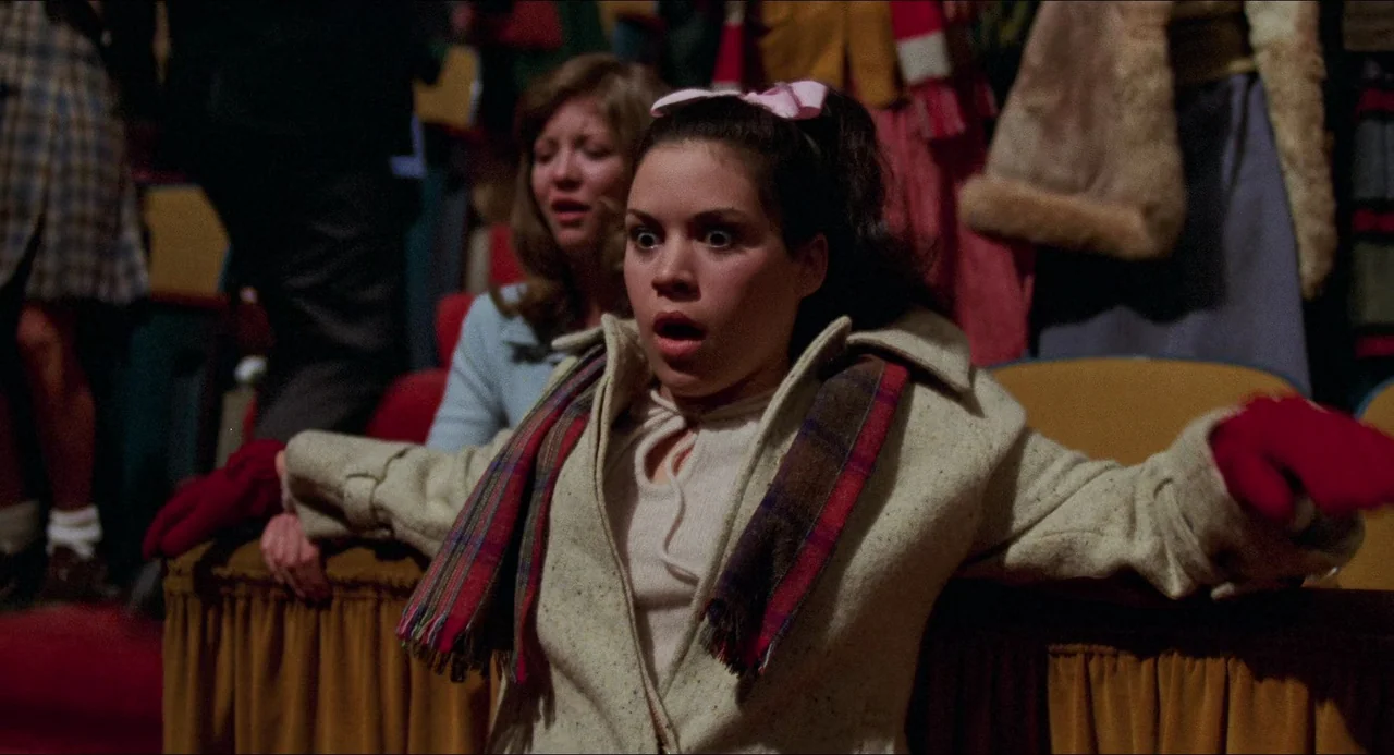 I Wanna Hold Your Hand (1978) movie still: medium — An auditorium interior with rows of padded seats filled with people in winter attire. A woman…