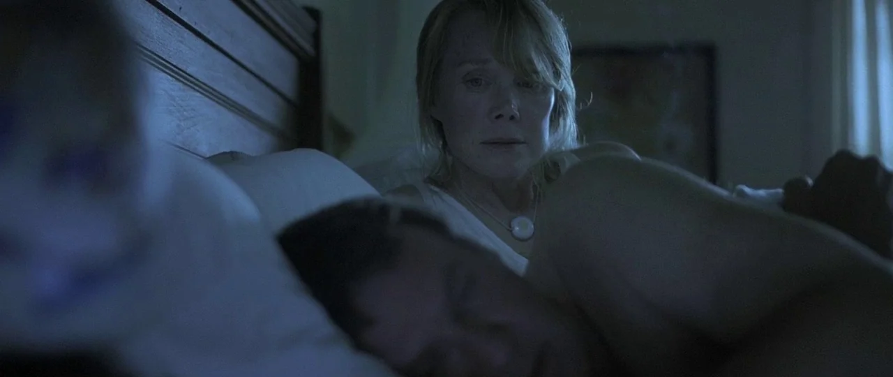 In the Bedroom (2001) movie still: medium — A dark, dimly lit indoor setting featuring a couple lying in bed at night. A woman stares toward a…