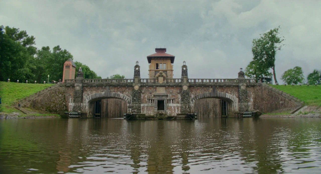 Jojo Rabbit (2019) movie still: establishing — A historic stone canal lock with two large arched openings stands above a river. The structure…