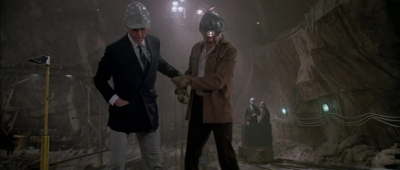 A View to a Kill (1985) movie still: fullbody — An underground mining tunnel features rugged rock walls and industrial lighting throughout the…
