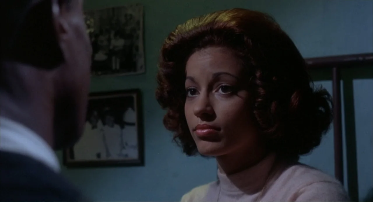 Cooley High (1975) movie still: medium — A dimly lit room features a green wall adorned with two framed photographs. A woman with voluminous hair…
