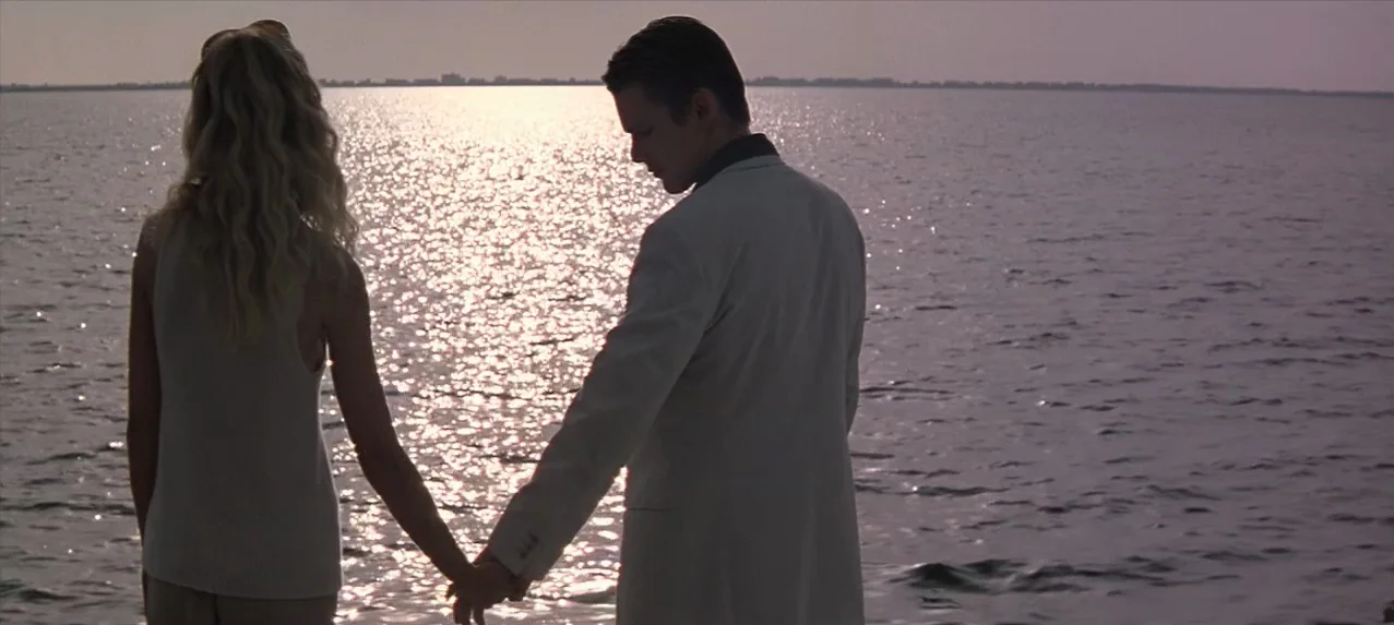 Great Expectations (1998) movie still: medium — A man and woman stand together at the edge of the water at dusk. They hold hands while facing the…