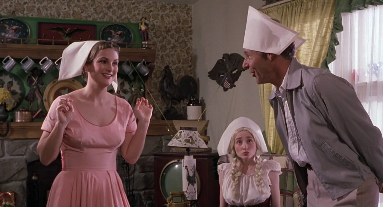 Cry Baby (1990) movie still: medium — A 1950s interior with floral wallpaper, stone fireplace, and rustic Americana decorative elements. Three…