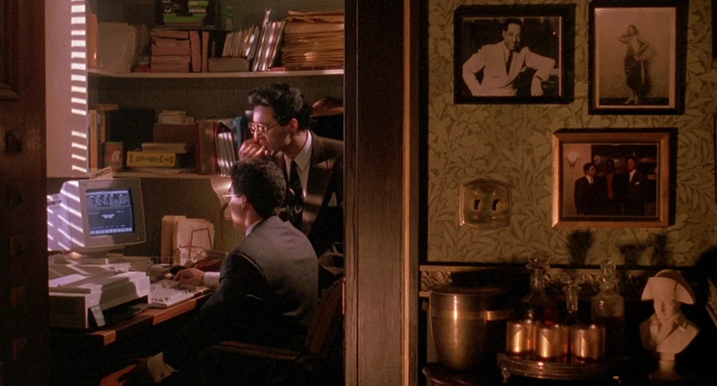 Mo’ Better Blues (1990) movie still: medium — A cluttered room features patterned green wallpaper, framed wall portraits, and a desk workspace. Two…