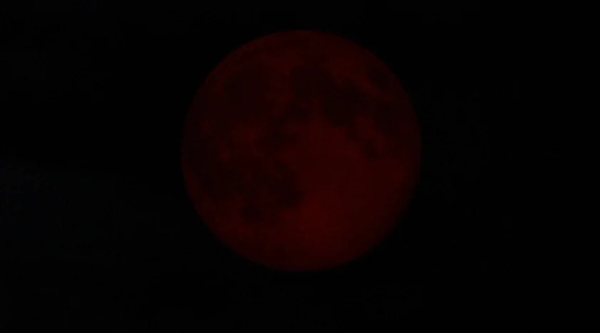 The House Of The Devil (2009) movie still: closeup — A dark, expansive night sky contains a large, glowing red celestial sphere. The circular object…