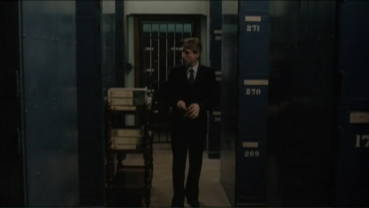 The Gathering Storm (2002) movie still: medium — An archive room is lined with tall, numbered blue metal storage lockers. A man in a suit stands in…