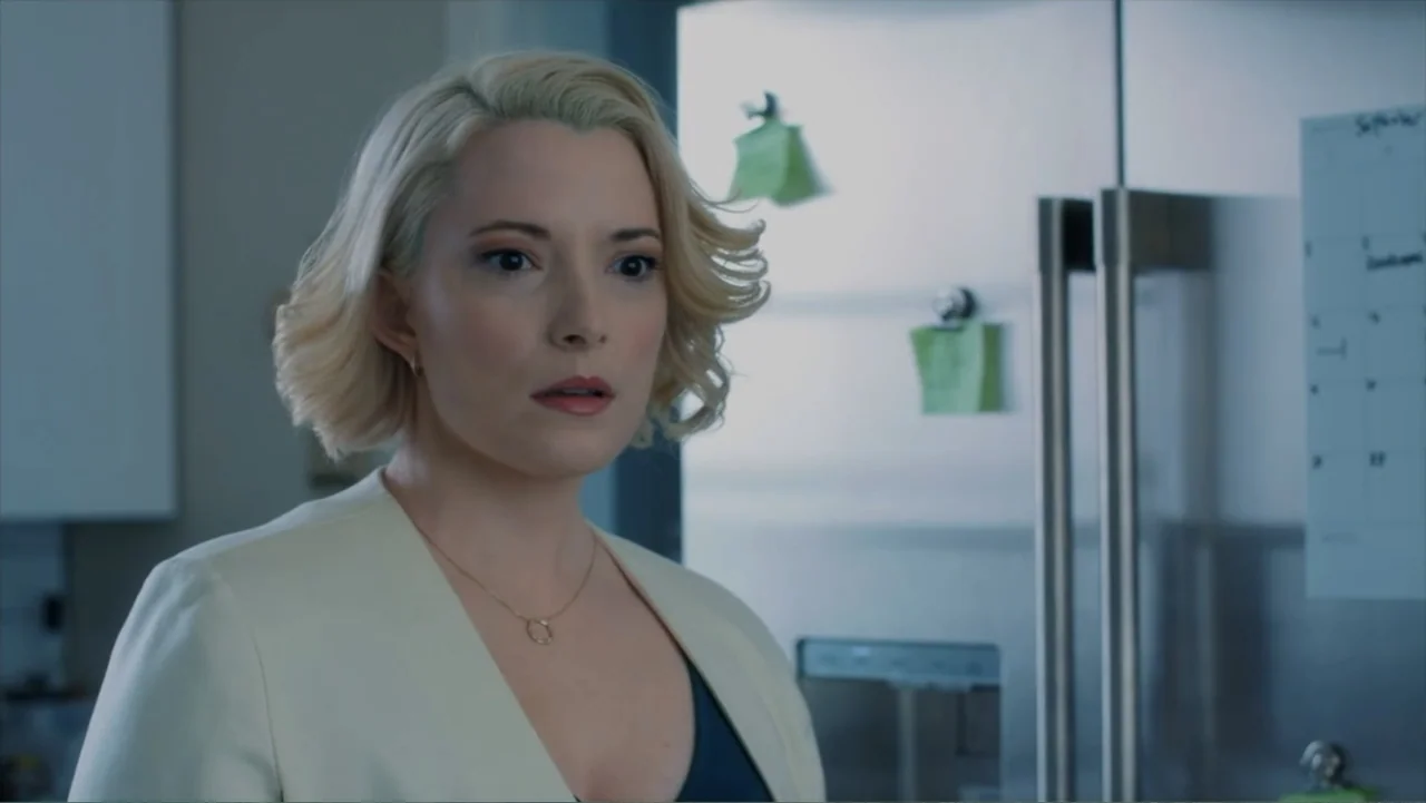 Storm Damage (2000) movie still: medium — A modern domestic kitchen with a stainless steel refrigerator and a wall calendar. A woman in a blazer…