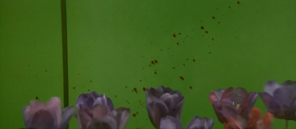 Dune (1984) movie still: closeup — A green wall features a series of scattered red liquid droplets across its surface. A cluster of dark purple…
