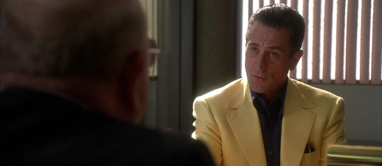 Casino (1995) movie still: medium — An office with vertical blinds covering a window providing bright backlighting. A man in a yellow jacket sits…