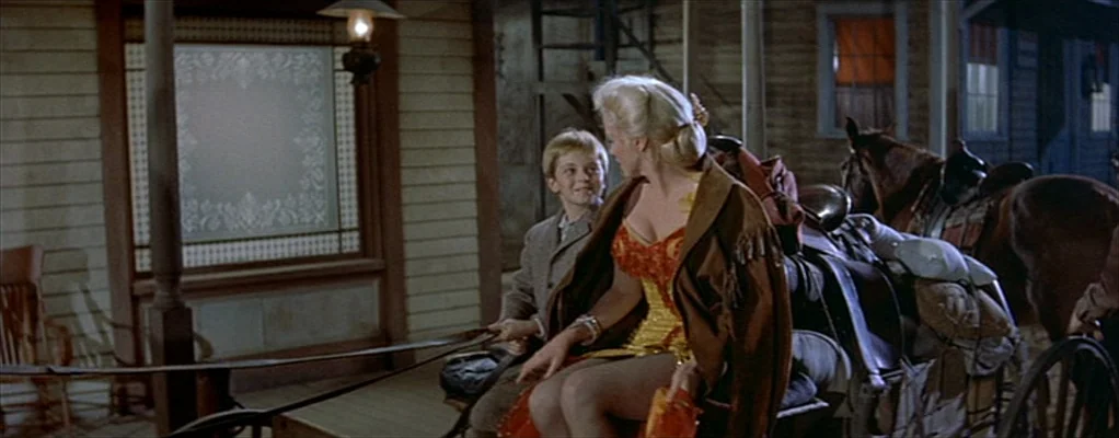 River of No Return (1954) movie still: medium — A wooden building porch is equipped with a hanging light fixture and seating. A young boy sits next…