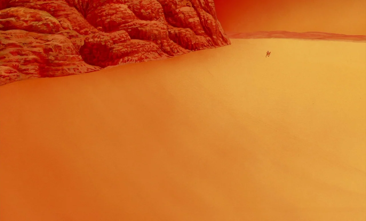 Aladdin (1992) movie still: establishing — A vast arid landscape features orange sand dunes beneath a bright orange sky. A jagged red rock formation…