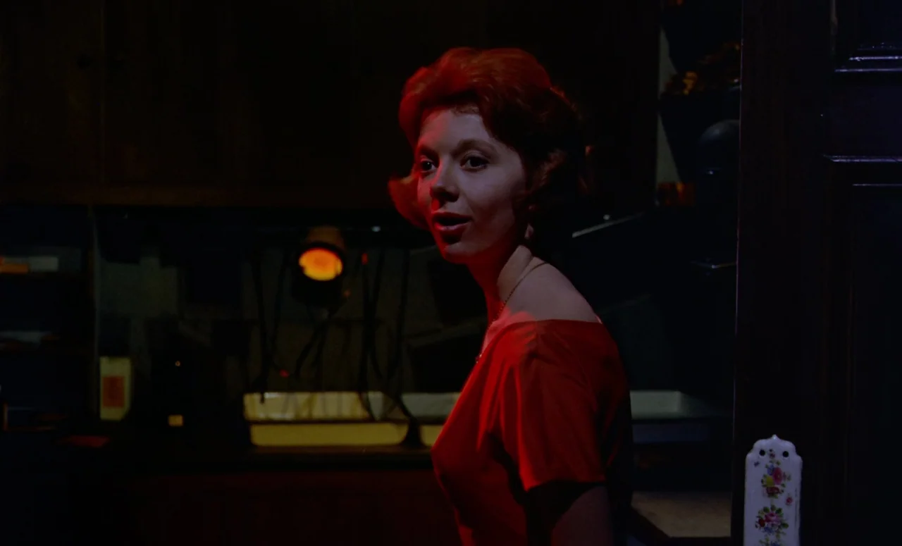 Peeping Tom (1960) movie still: medium — A dimly lit room with dark wooden furniture and an illuminated warm light source. A woman with red hair…