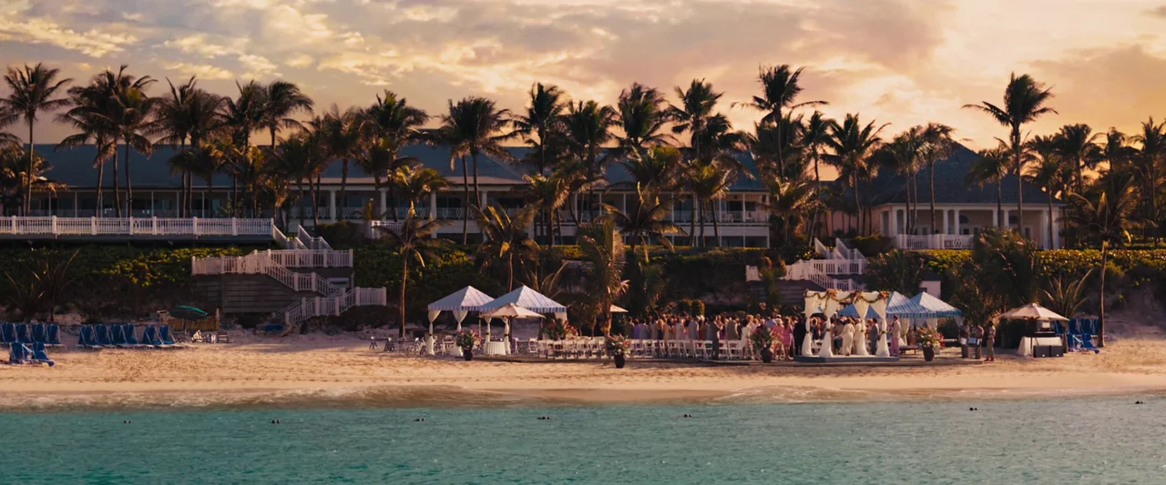 The Wolf of Wall Street (2013) movie still: wide — A luxury beach resort features palm trees and white buildings above a sandy shoreline. A wedding…