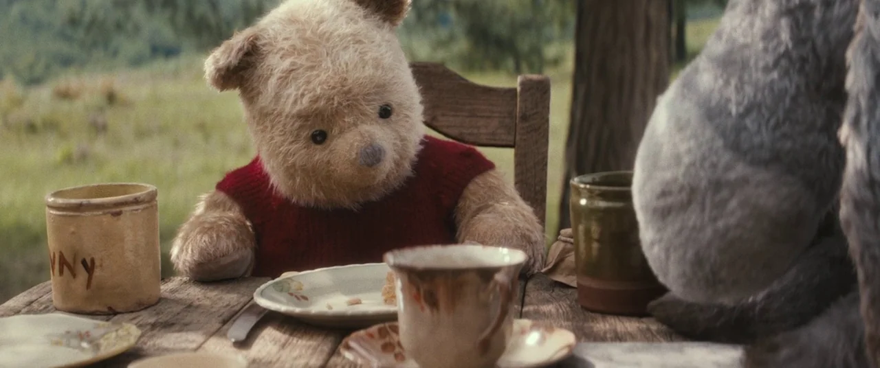 Christopher Robin (2018) movie still: medium — A rustic wooden table is set outdoors with ceramic dishware and a honey pot. A stuffed bear in a red…