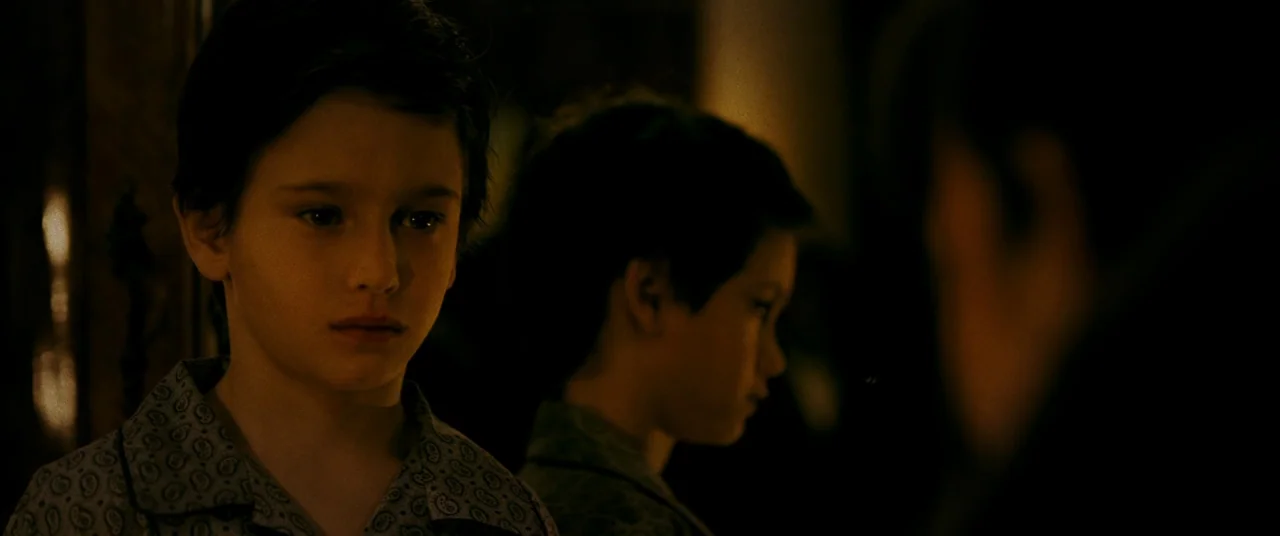Ready or Not (2019) movie still: closeup — A dark indoor space where a young boy observes himself in a dimly lit mirror. The boy wears pajamas and…