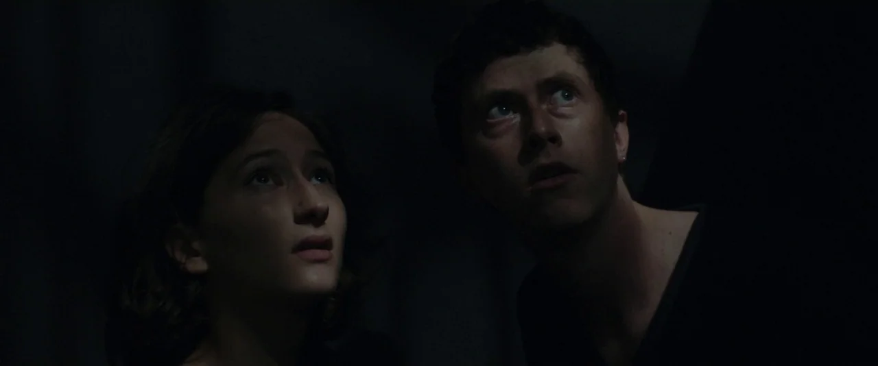 Nocturama (2016) movie still: medium — Two individuals stand in a dark, poorly lit space with black surroundings. They look upwards with focused…
