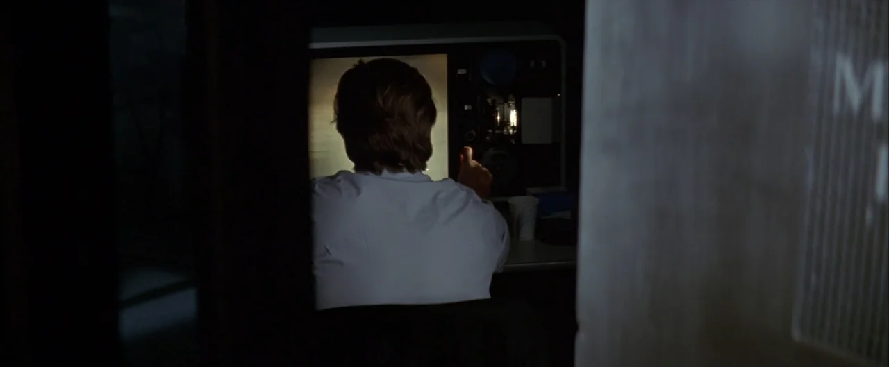 Arlington Road (1999) movie still: medium — A dark, cramped space containing a specialized mechanical film viewing and editing device. A man in a…