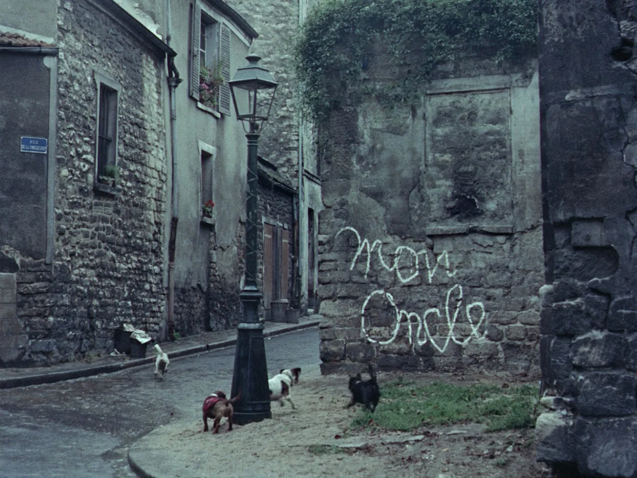 Mon Oncle (1958) movie still: wide — A narrow European urban street features aged stone buildings and a vintage wrought-iron lamppost. The words Mon…