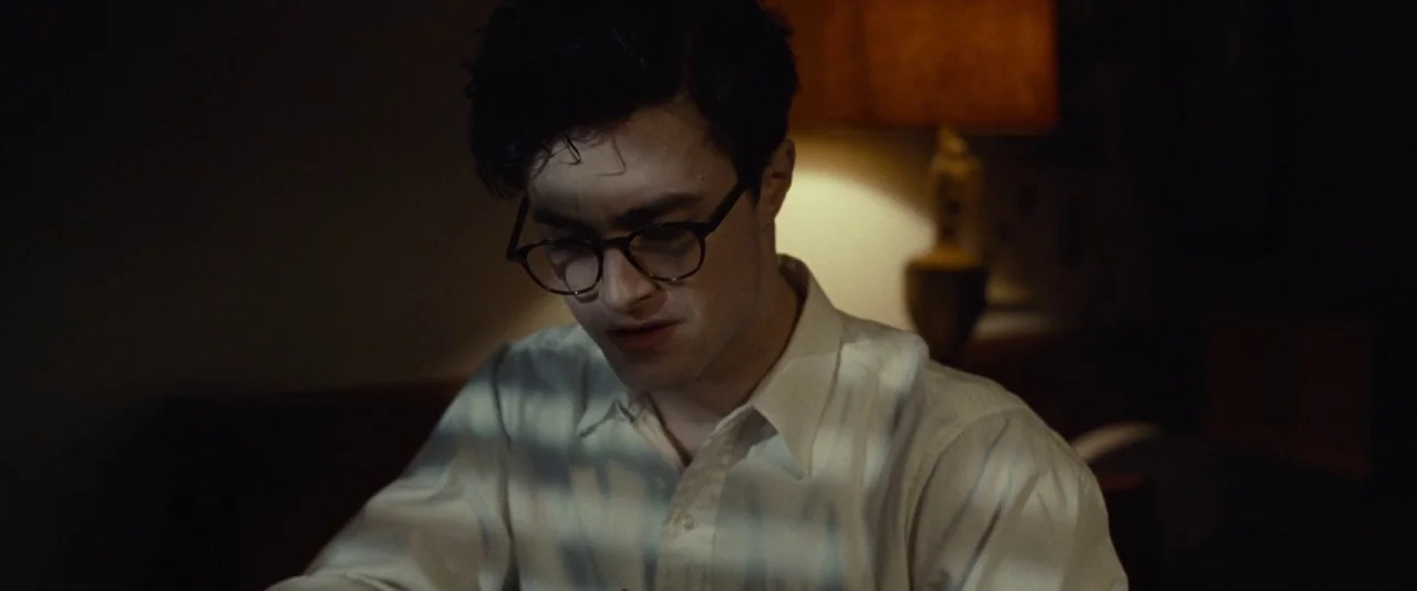 Kill Your Darlings (2013) movie still: medium — A dimly lit space features a man sitting before a soft light source. The man looks downward with…