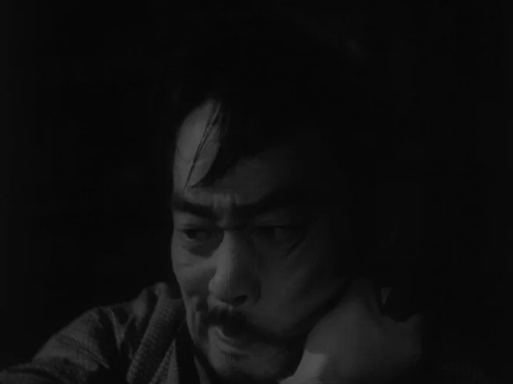 Sanshiro Sugata (1943) movie still: closeup — The interior of a darkened room with no background details visible. A man rests his head on his hand…