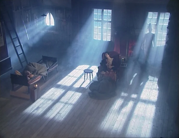 In The Presence of a Clown (1997) movie still: wide — An attic room with wooden floors contains a cot and a single armchair. Haze fills the air as…