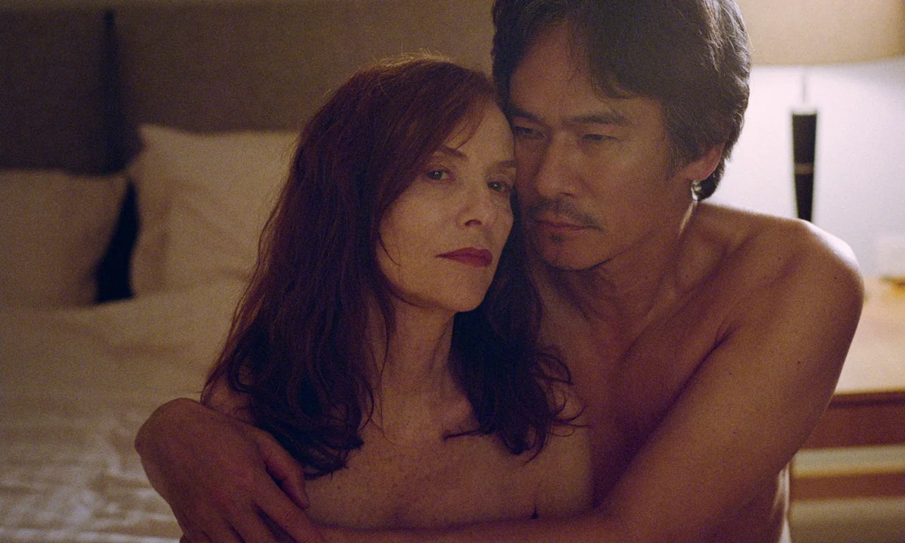Sidonie in Japan (2023) movie still: medium — A dimly lit indoor space with a soft light source on a side table. A man and a woman sit together on a…