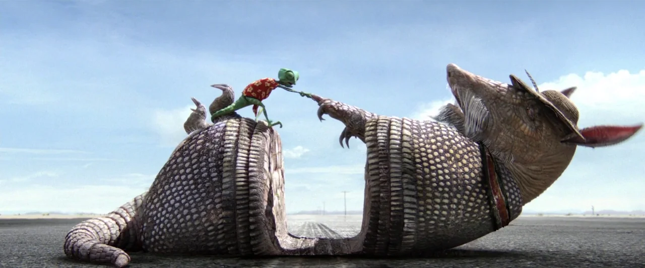 Rango (2011) movie still: wide — A flat asphalt road stretches across an arid desert landscape under a clear sky. A small chameleon stands on a…