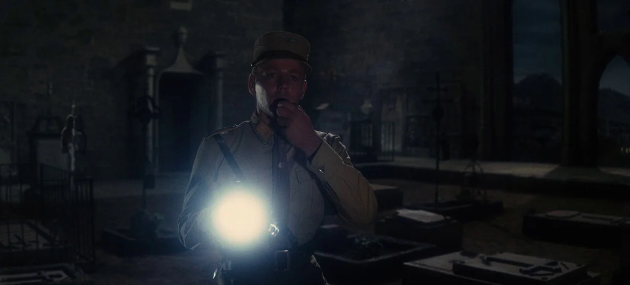 The Sound of Music (1965) movie still: medium — A man in a military uniform explores a dark cemetery at night with a flashlight. Stone gravestones…