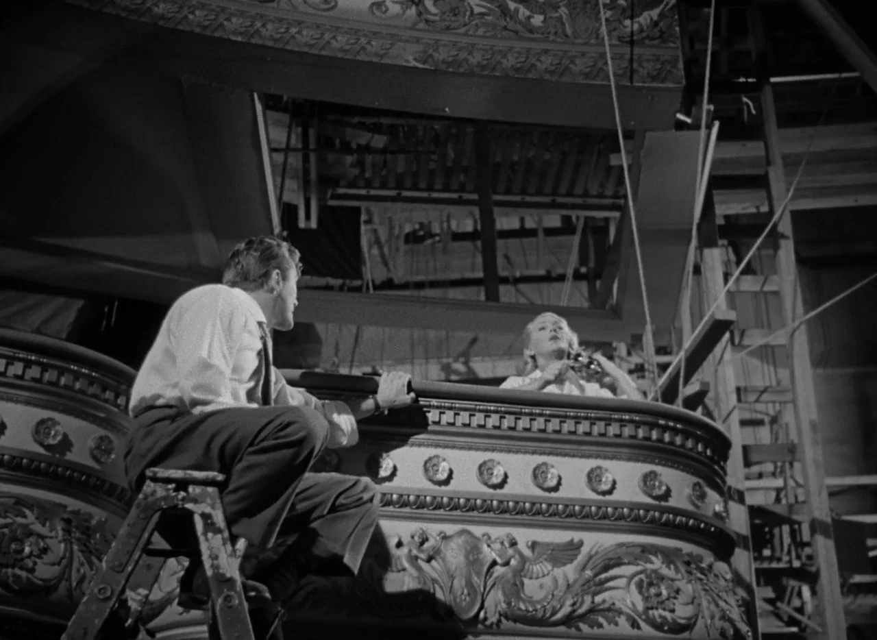 The Bad and the Beautiful (1952) movie still: medium — A dark balcony featuring ornate plaster carvings with a ladder placed near the railing. A man…