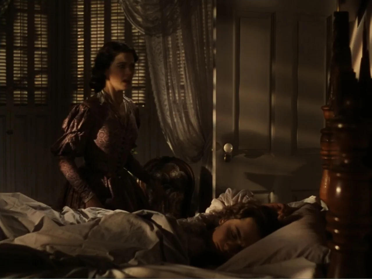 Gone with the Wind (1939) movie still: medium — A dimly lit room features a four-poster bed and closed shutters over the windows. One woman stands…