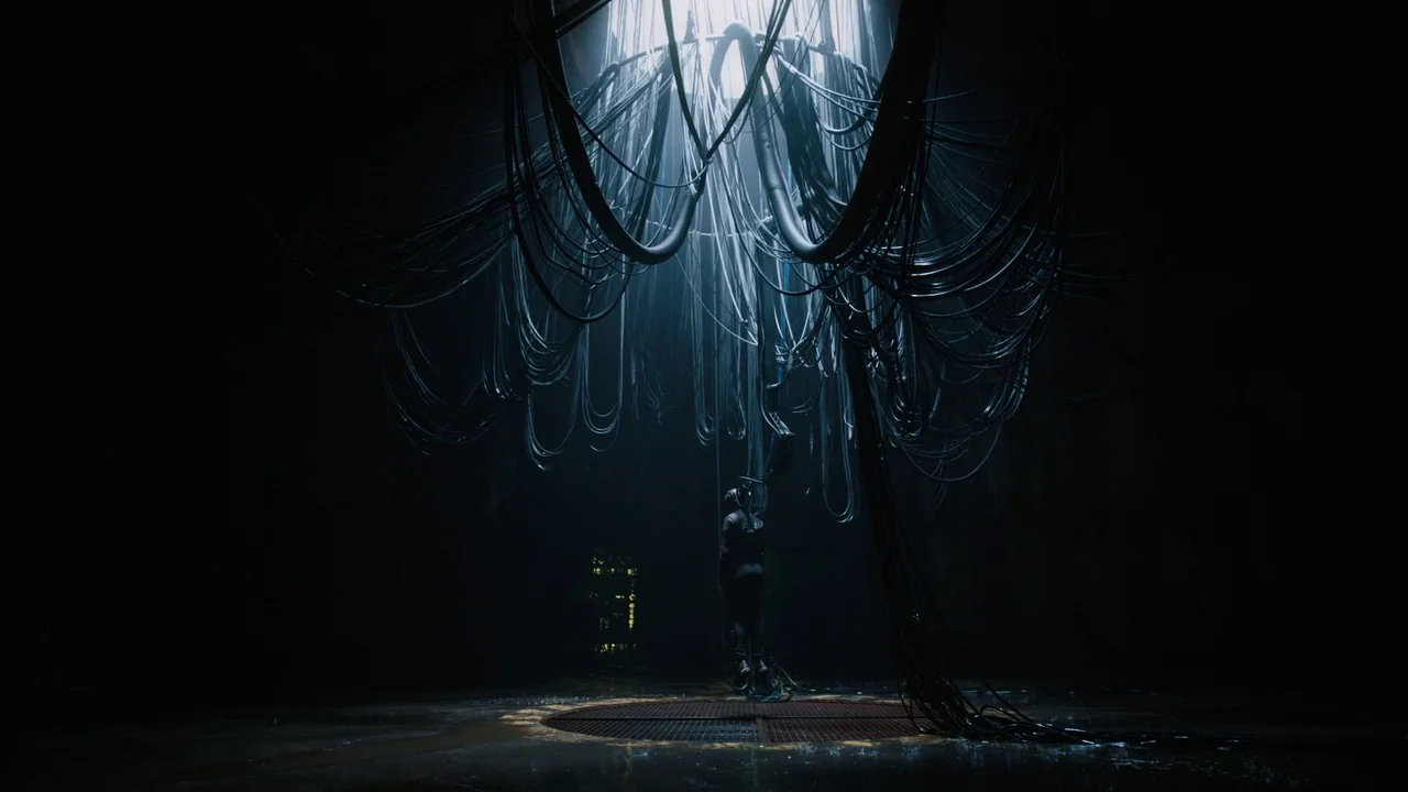 Ghost in the Shell (2017) movie still: wide — A dark subterranean circular room contains a central metal grate on the floor. Numerous black cables…