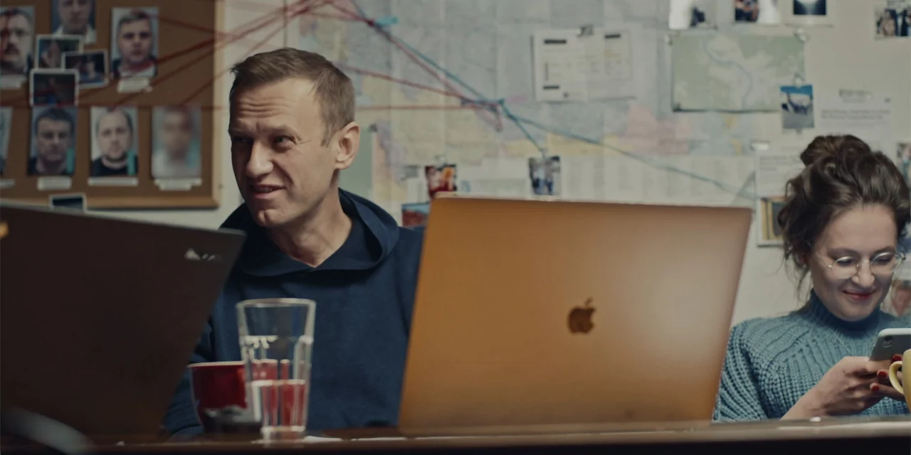 Navalny (2022) movie still: medium — An office room features a large investigation map on the back wall covered in pins. A man in a hoodie and a…