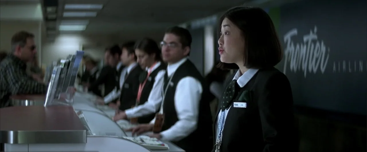 Enough (2002) movie still: medium — An airline service desk features a row of employees standing behind white computer terminals. A young female…