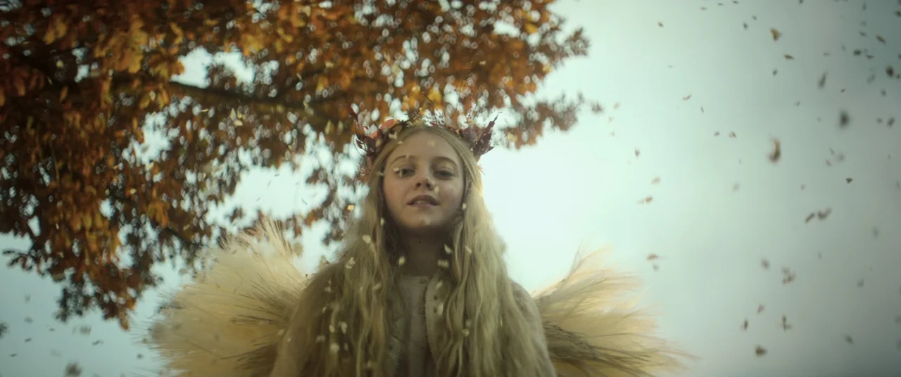 Lord of Misrule (2023) movie still: medium — A young girl stands in an open area during autumn with falling dry leaves. She wears a floral wreath on…