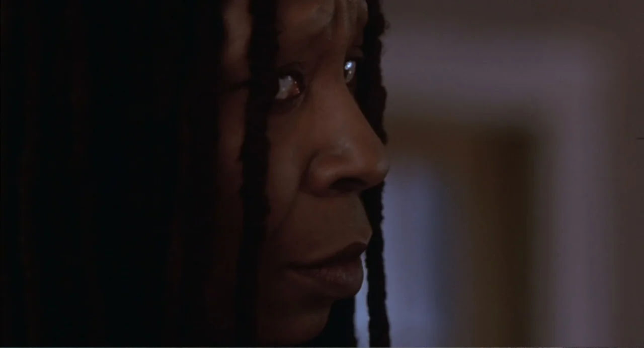 Bogus (1996) movie still: closeup — A dimly lit interior room at night with deep shadows obscuring most surroundings. A woman in profile looks…