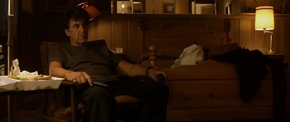 The Insider (1999) movie still: medium — A dimly lit motel room features wood-paneled walls and a wooden bed frame. An older man sits in a chair…
