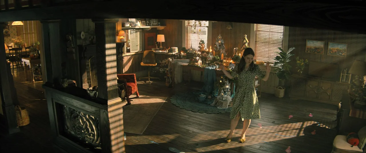 No One Will Save You (2023) movie still: wide — A living room filled with miniature village models displayed on a large wooden table. A young woman…