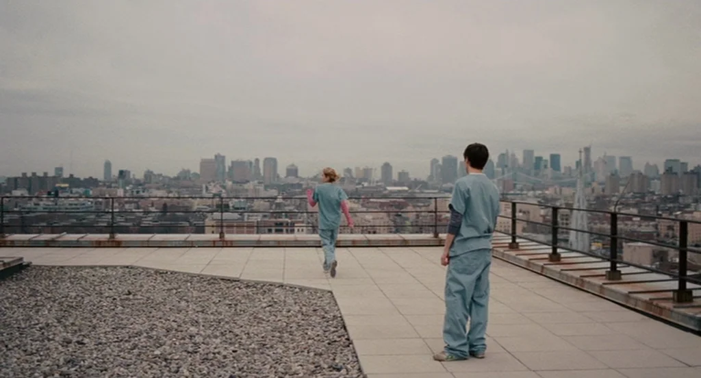 It’s Kind Of A Funny Story (2010) movie still: wide — A flat rooftop with paved walkways and gravel patches overlooking a sprawling city skyline. A…