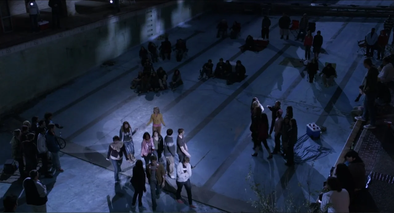 Pitch Perfect (2012) movie still: wide — A large concrete swimming pool at night is filled with many young adults congregating. People sit on the…