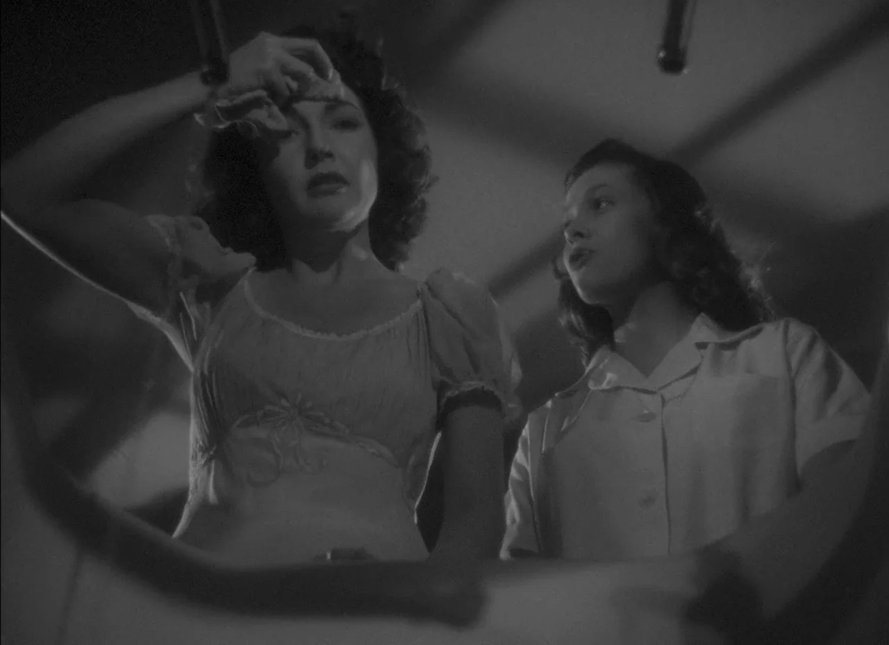 The Amazing Mr. X (1948) movie still: medium — A dark indoor space with overhead pipes visible against the ceiling structure. Two women look…