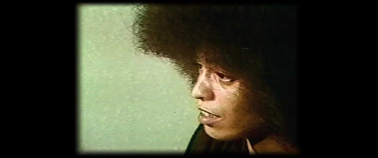Judas and the Black Messiah (2021) movie still: closeup — A close-up shot of a person with a large afro against a solid wall. The subject is…