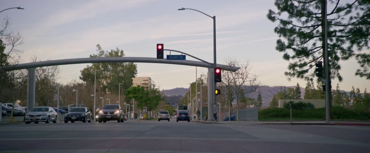 Bird Box (2018) movie still: wide — An urban intersection features a large arched sign structure overhead marked Smith St. Several cars wait at red…