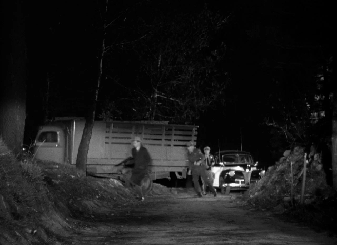 Out of the Past (1947) movie still: wide — A dark night scene shows a dirt road between two parked vehicles. Three men run past a truck and a patrol…