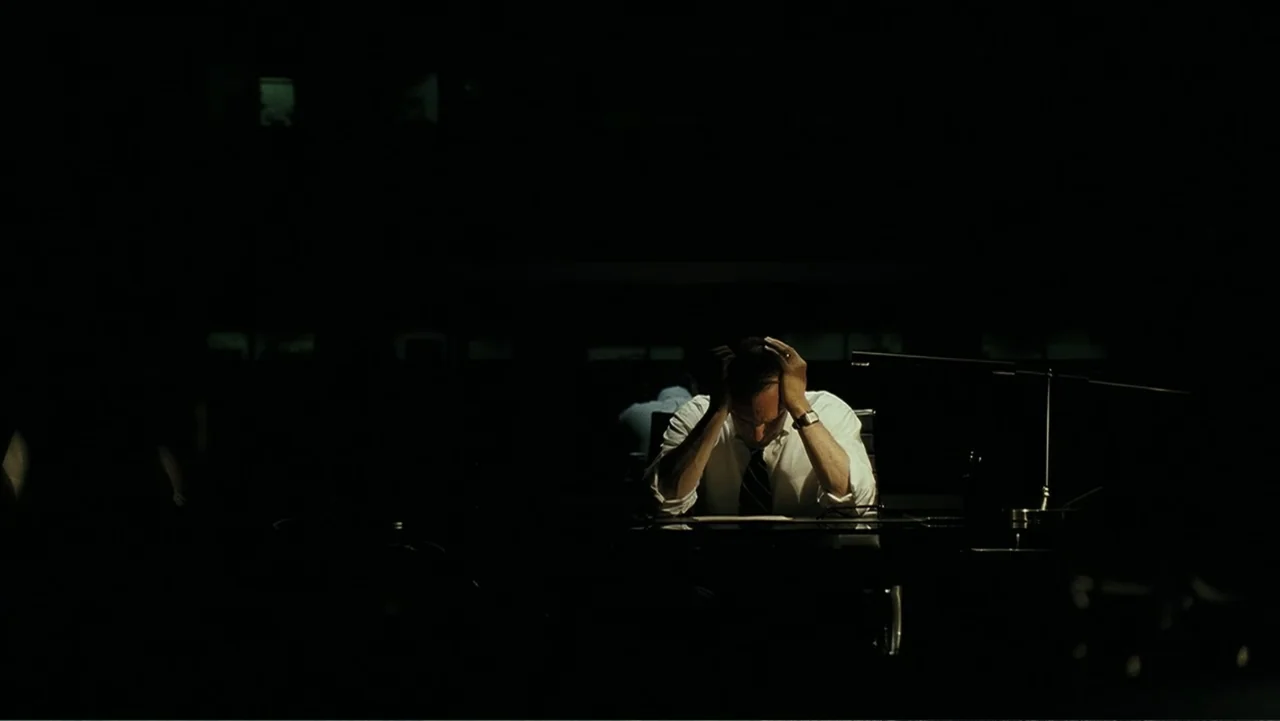 Mr. Brooks (2007) movie still: medium — A dimly lit office at night dominated by dark, empty surroundings. A man sits at a desk with his hands…