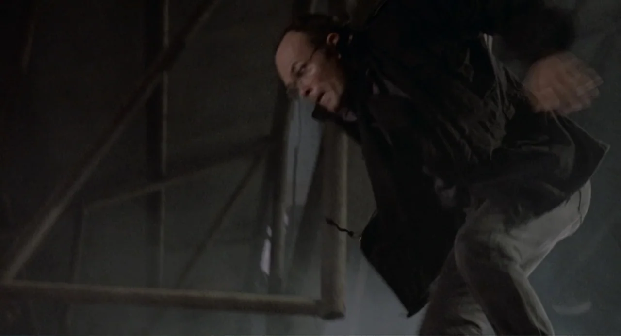 RoboCop (2014) movie still: medium — An interior space features exposed structural beams and dark, shadowed surroundings. A man moves quickly across…