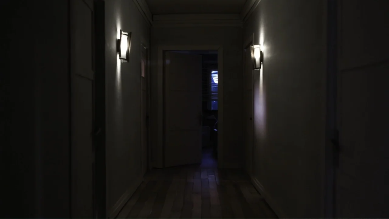 Bestia (2017) movie still: medium — A dark, narrow indoor corridor features light-colored walls and wood-patterned flooring. Two illuminated wall…