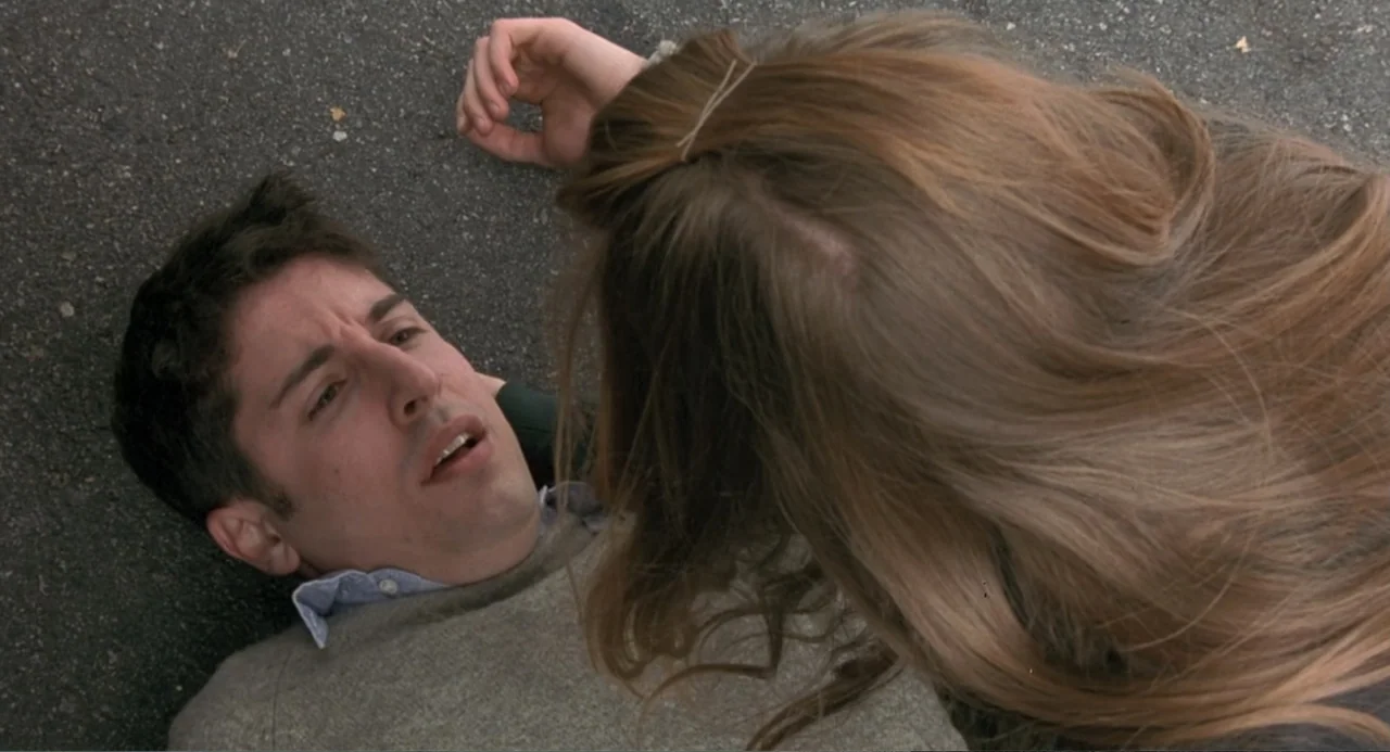Wedding Daze (2006) movie still: medium — A dark asphalt surface serves as the background for two individuals lying together. A man lies on his back…